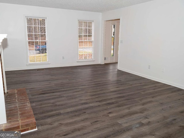 empty room featuring a textured ceiling, a brick fireplace, and dark hardwood / wood-style floors