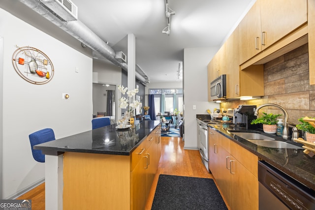 kitchen with light hardwood / wood-style flooring, stainless steel appliances, track lighting, dark stone countertops, and sink