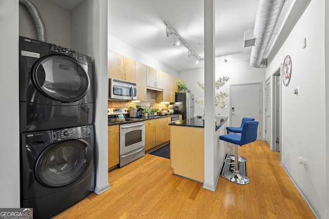 kitchen with stacked washer and dryer, stainless steel appliances, light hardwood / wood-style floors, and light brown cabinets