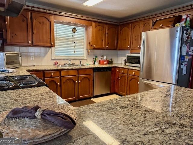 kitchen featuring stainless steel appliances, light stone countertops, sink, range hood, and tasteful backsplash