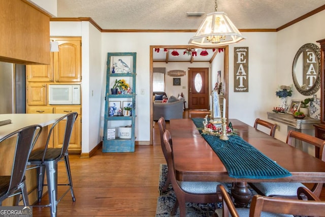 dining room with an inviting chandelier, a textured ceiling, ornamental molding, and hardwood / wood-style flooring