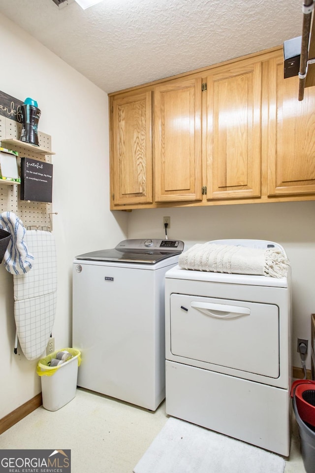 clothes washing area with independent washer and dryer, a textured ceiling, and cabinets