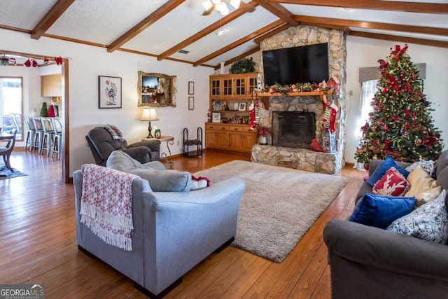 living room featuring vaulted ceiling with beams, wood-type flooring, and a stone fireplace