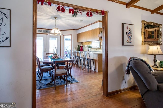 dining space featuring a textured ceiling, french doors, wood-type flooring, ornamental molding, and beamed ceiling