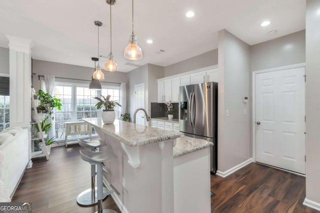 kitchen featuring a center island with sink, hanging light fixtures, a breakfast bar, stainless steel refrigerator with ice dispenser, and white cabinets