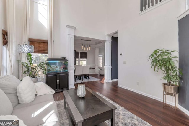 living room featuring a towering ceiling, decorative columns, dark wood-type flooring, and a chandelier