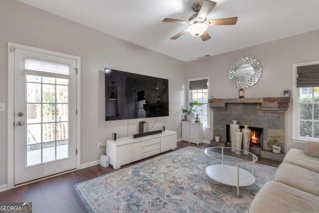 living room featuring a fireplace, dark wood-type flooring, ceiling fan, and a healthy amount of sunlight