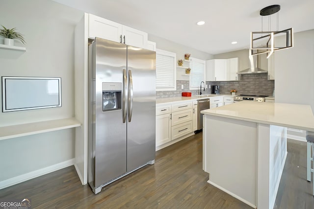 kitchen featuring appliances with stainless steel finishes, pendant lighting, wall chimney range hood, and white cabinets