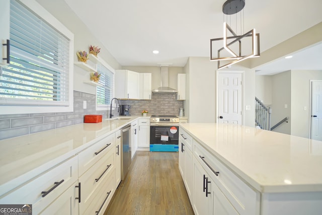 kitchen featuring hanging light fixtures, stainless steel appliances, wall chimney range hood, backsplash, and white cabinets