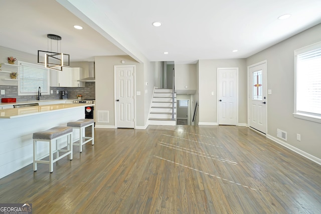 kitchen featuring a breakfast bar area, hanging light fixtures, dark wood-type flooring, white cabinetry, and wall chimney range hood