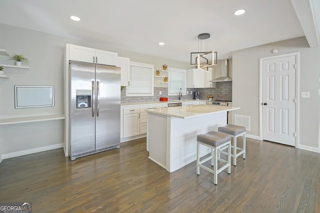 kitchen with hanging light fixtures, stainless steel appliances, wall chimney range hood, a kitchen island, and white cabinets