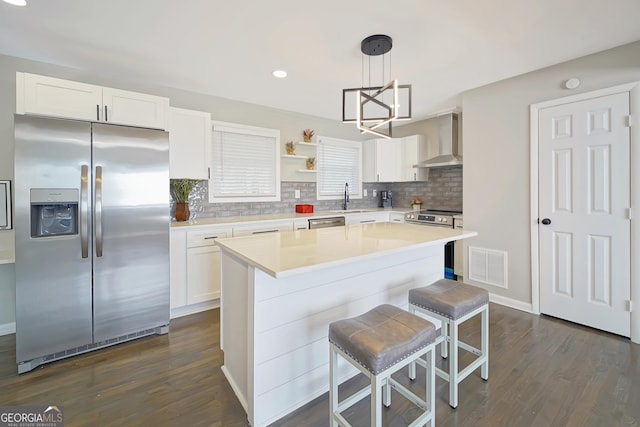 kitchen with stainless steel appliances, hanging light fixtures, a kitchen island, sink, and wall chimney range hood