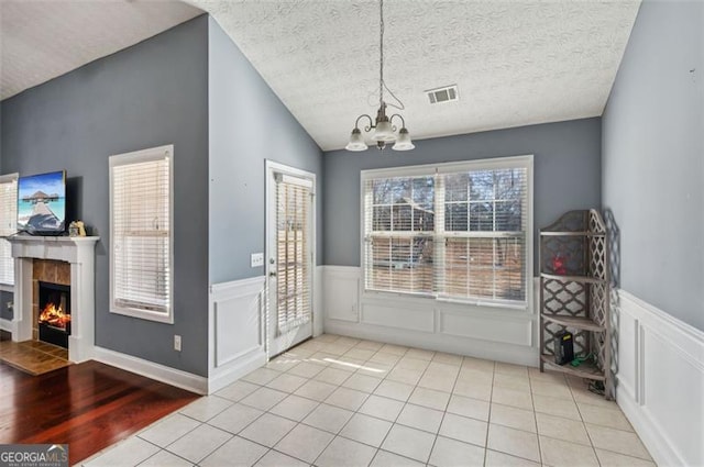 unfurnished dining area featuring a textured ceiling, a chandelier, a tile fireplace, light tile patterned floors, and lofted ceiling