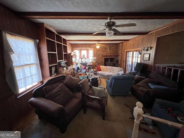 living room featuring wooden walls, a textured ceiling, a fireplace, beamed ceiling, and ceiling fan