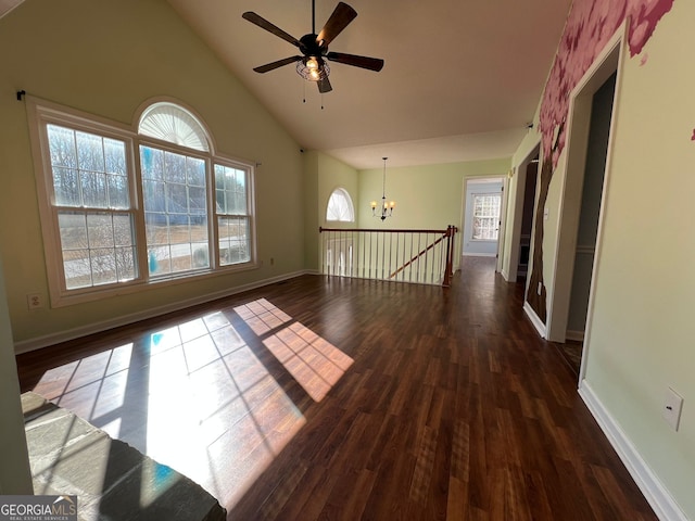 unfurnished room with ceiling fan with notable chandelier, a healthy amount of sunlight, dark hardwood / wood-style floors, and high vaulted ceiling