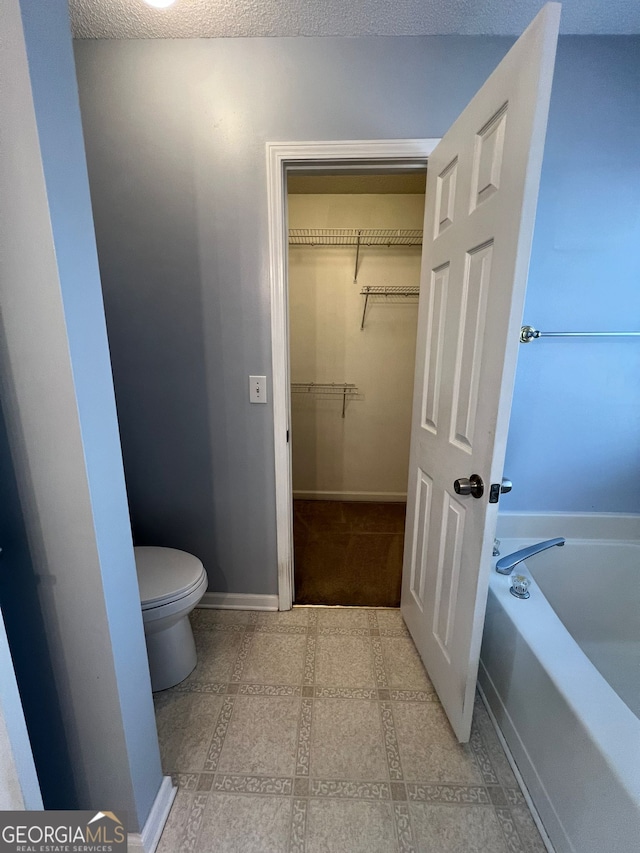 bathroom featuring a bath, a textured ceiling, and toilet