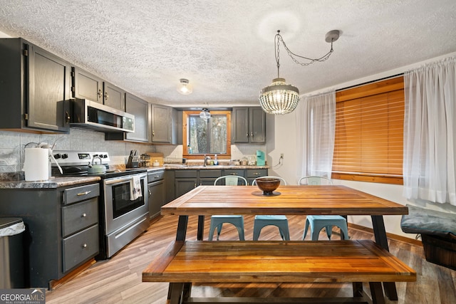 kitchen with stainless steel appliances, light wood-type flooring, gray cabinets, a chandelier, and pendant lighting