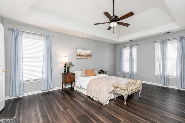 bedroom featuring multiple windows, ceiling fan, a tray ceiling, and dark hardwood / wood-style floors