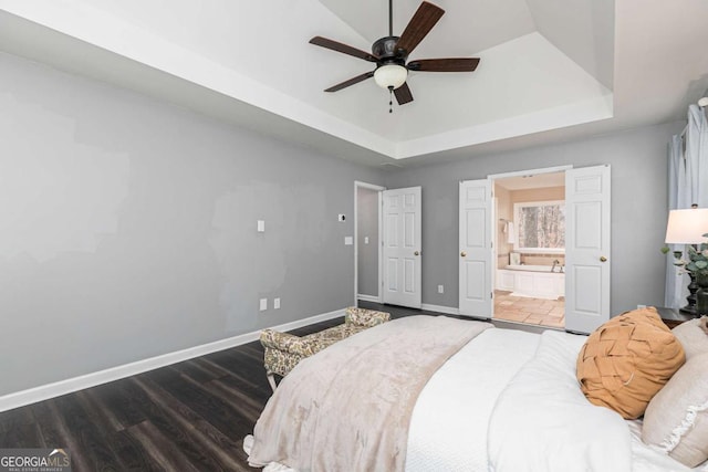 bedroom with connected bathroom, dark hardwood / wood-style flooring, ceiling fan, and a tray ceiling