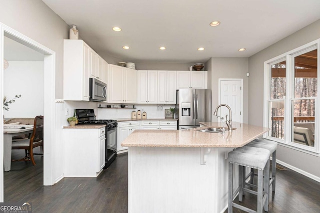 kitchen with a center island with sink, a breakfast bar, white cabinetry, appliances with stainless steel finishes, and sink