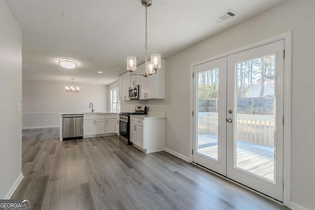 kitchen with kitchen peninsula, appliances with stainless steel finishes, pendant lighting, and white cabinetry