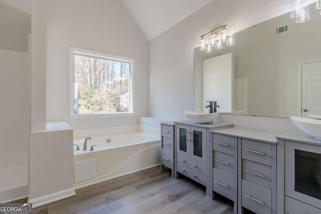 bathroom featuring hardwood / wood-style flooring, vaulted ceiling, a tub to relax in, and vanity