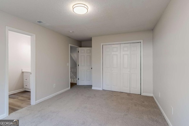 unfurnished bedroom with a textured ceiling, light colored carpet, and a closet