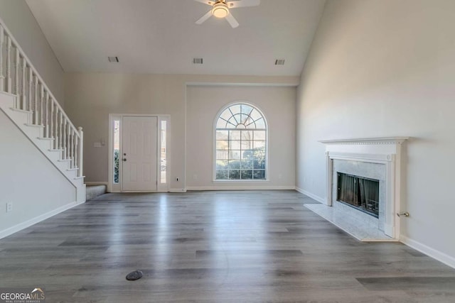 unfurnished living room with a high end fireplace, a high ceiling, dark hardwood / wood-style flooring, and ceiling fan