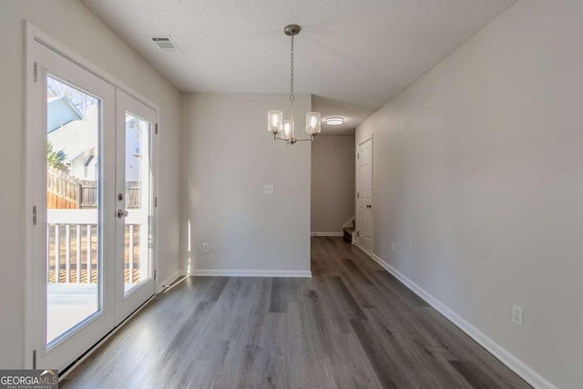 unfurnished dining area with a textured ceiling, a chandelier, and dark hardwood / wood-style floors