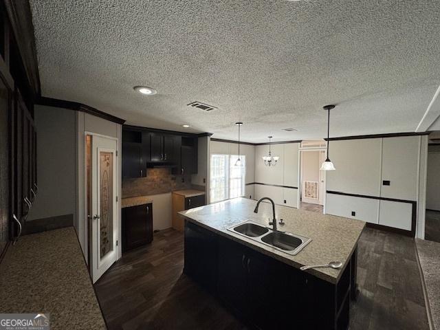 kitchen with decorative light fixtures, an island with sink, an inviting chandelier, dark hardwood / wood-style flooring, and sink