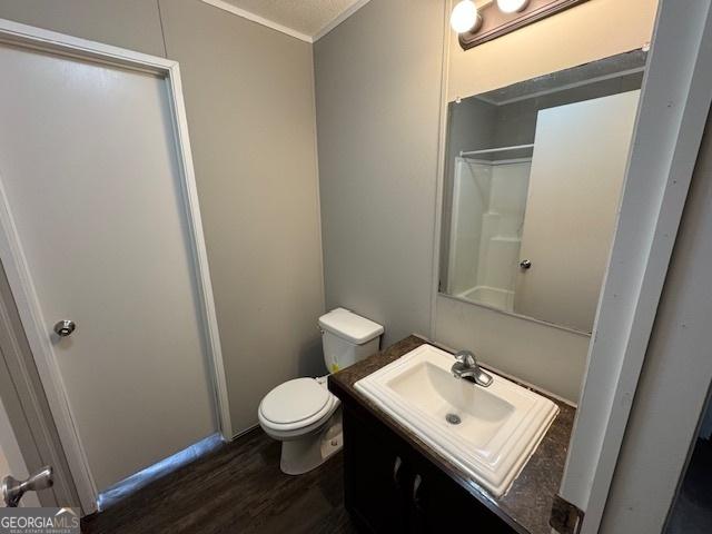 bathroom with hardwood / wood-style floors, ornamental molding, toilet, walk in shower, and vanity