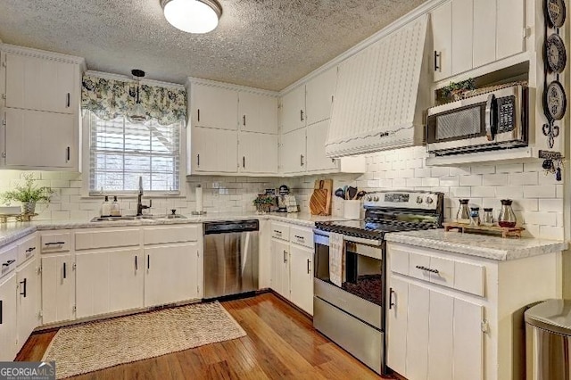 kitchen with sink, white cabinetry, light hardwood / wood-style floors, hanging light fixtures, and appliances with stainless steel finishes