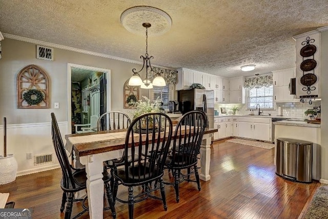 dining space featuring a textured ceiling, dark wood-type flooring, an inviting chandelier, and crown molding