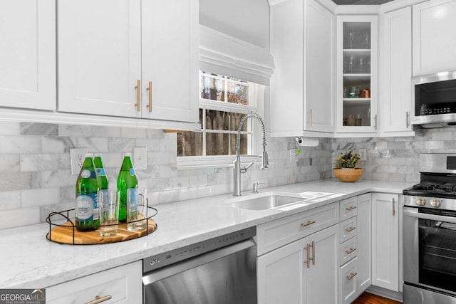 kitchen with appliances with stainless steel finishes, light stone counters, sink, white cabinetry, and backsplash