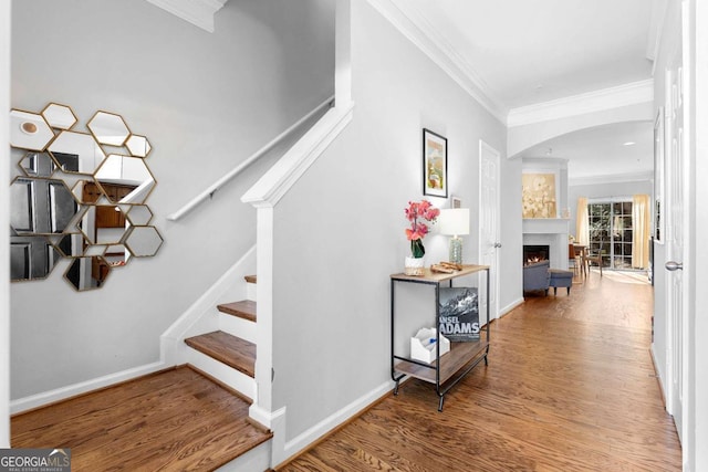 stairway featuring a large fireplace, crown molding, and wood-type flooring