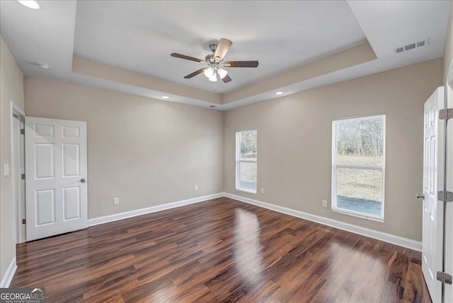 empty room with ceiling fan, a tray ceiling, and dark hardwood / wood-style floors