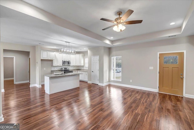 kitchen featuring decorative light fixtures, white cabinetry, light stone counters, an island with sink, and appliances with stainless steel finishes