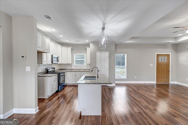 kitchen with appliances with stainless steel finishes, an island with sink, light stone counters, sink, and white cabinetry