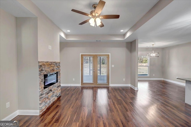 unfurnished living room featuring ceiling fan with notable chandelier, a raised ceiling, a fireplace, and dark hardwood / wood-style floors