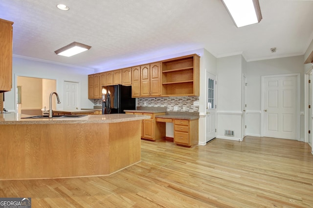 kitchen with kitchen peninsula, black fridge, light wood-type flooring, crown molding, and sink