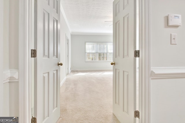 hallway featuring a textured ceiling, ornamental molding, and light colored carpet