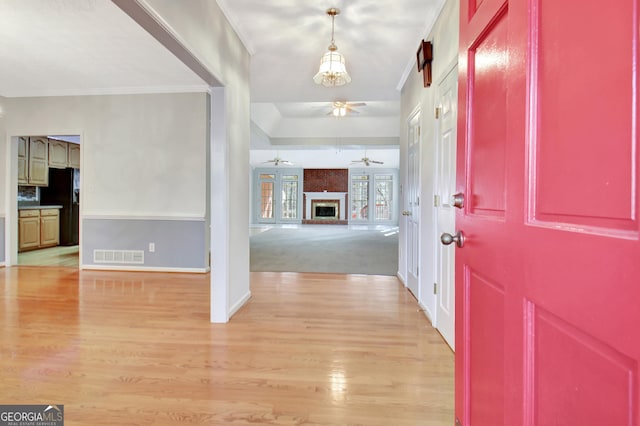 foyer entrance featuring light wood-type flooring, a large fireplace, and crown molding