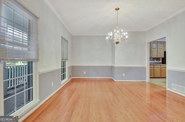 spare room featuring wood-type flooring, ornamental molding, and a notable chandelier