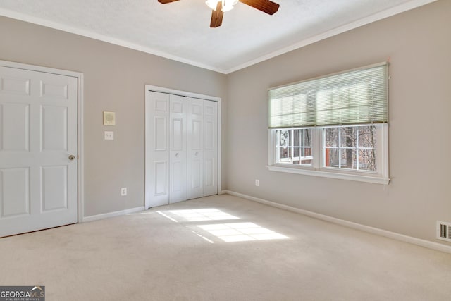 unfurnished bedroom with ceiling fan, light carpet, a closet, and crown molding