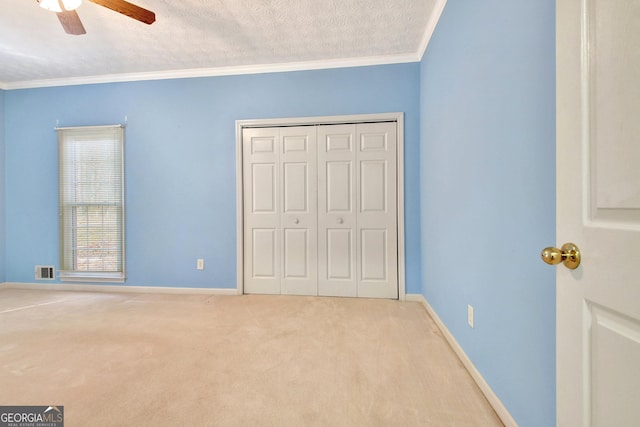 unfurnished bedroom with ceiling fan, a textured ceiling, carpet, and crown molding