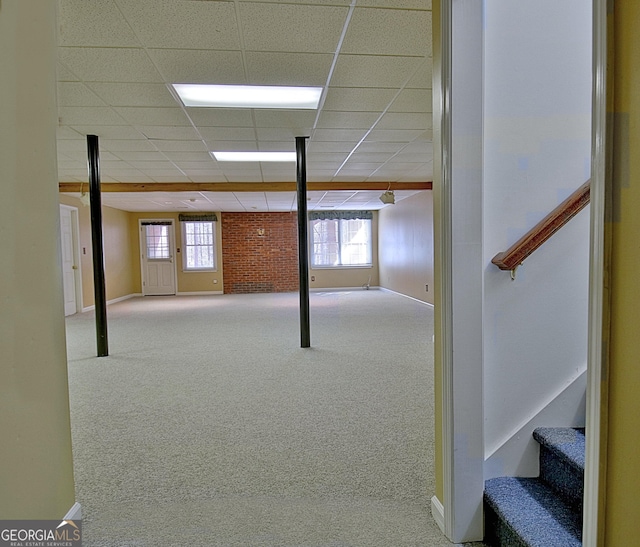 basement with brick wall, a paneled ceiling, and light carpet