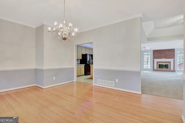 unfurnished dining area with light wood-type flooring, a fireplace, ceiling fan with notable chandelier, and ornamental molding