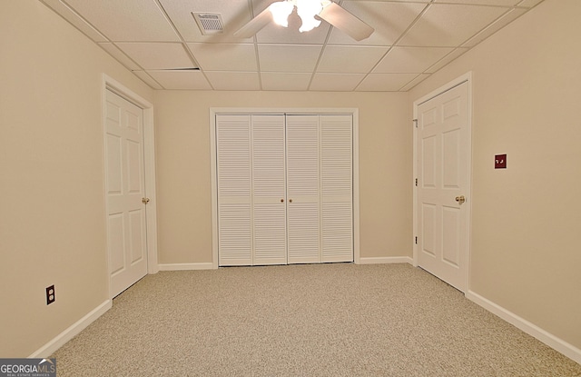 unfurnished bedroom with ceiling fan, a paneled ceiling, a closet, and carpet flooring