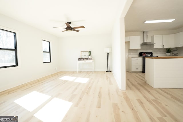 kitchen featuring ceiling fan, white cabinets, wall chimney exhaust hood, light hardwood / wood-style flooring, and black range with electric stovetop