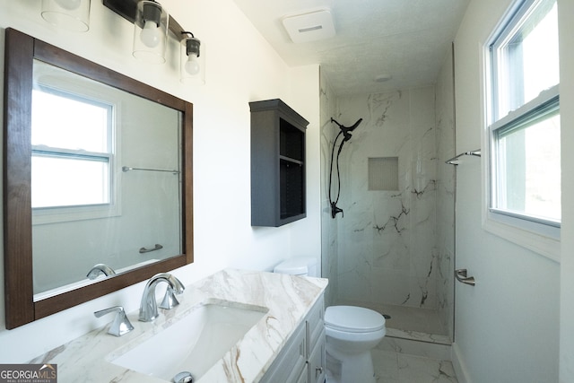 bathroom featuring toilet, vanity, plenty of natural light, and a tile shower